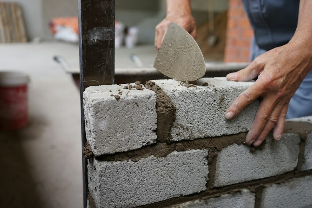 Mason applying mortar to a brick wall - stock photo by Solømen on Unsplash